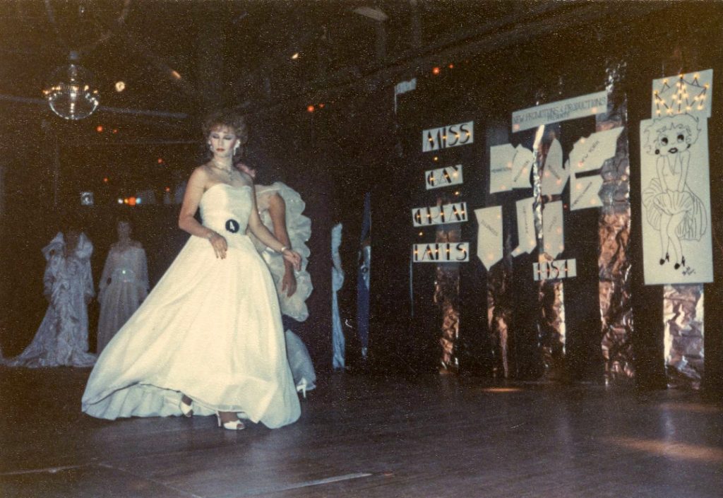 A drag performer walks across a stage.