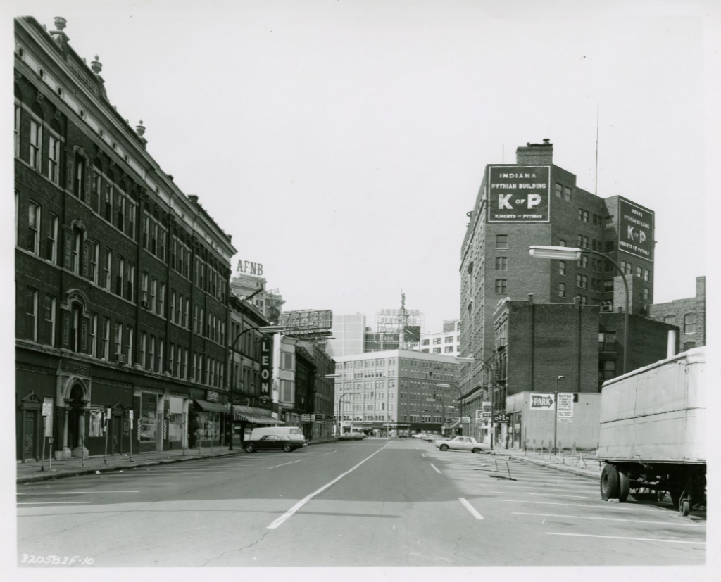 View looking down the middle of a city street. Buildings line either side of the street. At the end of the street is the rear of the 11-story Pythian Building.