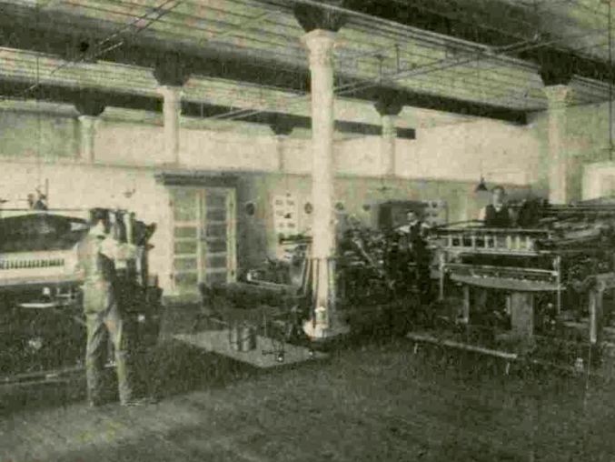 Two men work at separate printing presses in a large room.