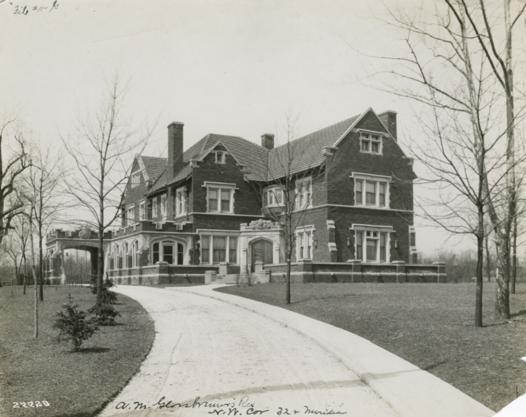 A large, ornate multistory home in the Jacobethan Revival–style. A long curved driveway leads up to the entrance of the house.
