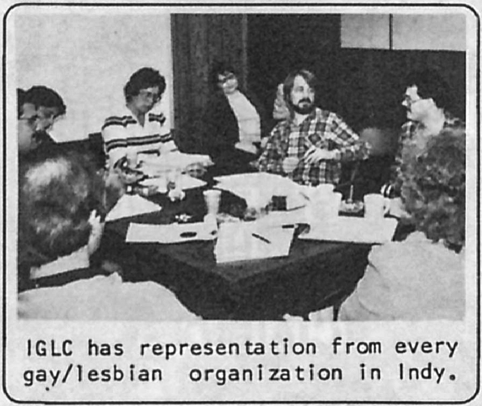 A group of people sit around a table. The table is strewn with papers. The text at the bottom of the photo reads "IGLC has representation from every gay/lesbian organization in Indy."