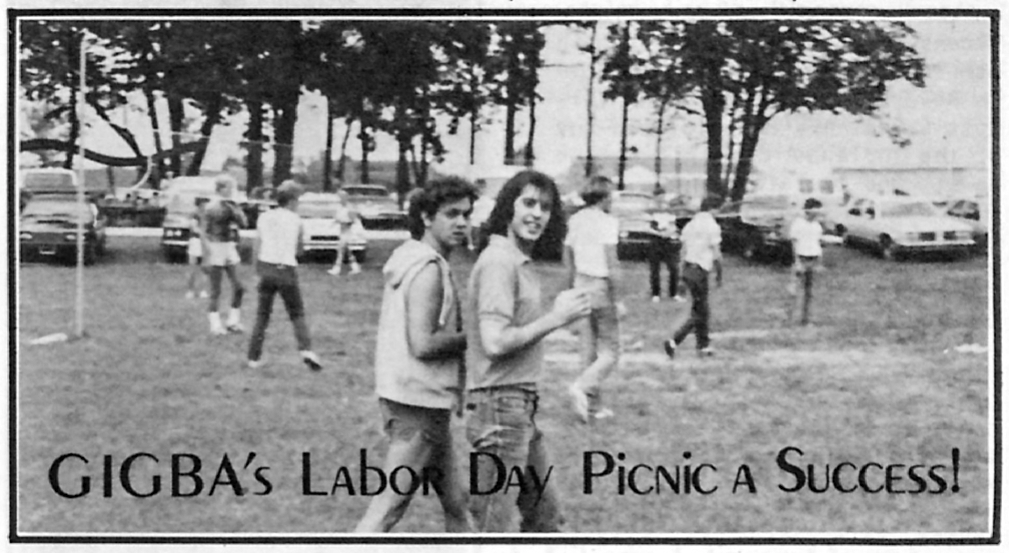 Two men walk together in the foreground. A group of men play volleyball in the background. Rows of cars are parked on the grass beyond the volleyball net. Text on the image reads "GIGBA's labor day picnic a success!"