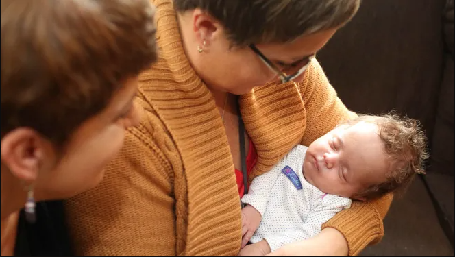 Two women look lovingly at a baby.