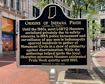 Indiana historical marker with the brick street of Monument Circle in the background. The marker's headline reads "Origins of Indiana Pride."