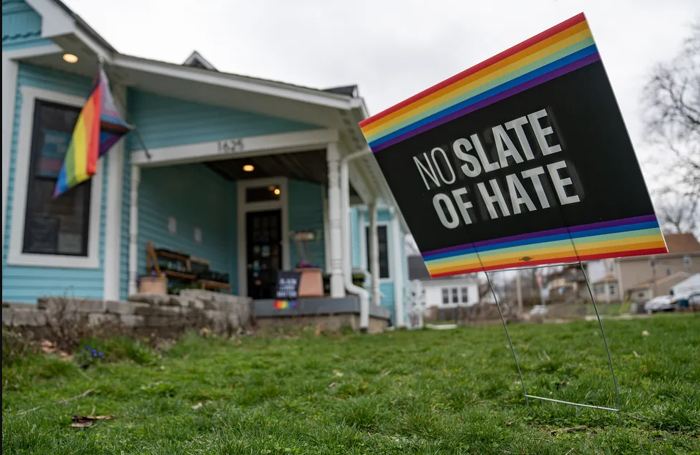 A yard sign placed outside of a residential looking building. The sign reads "No slate of hate" and has rainbow stripes on the top and bottom.
