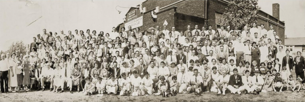 A large group of people are gathered together in front of a brick building.