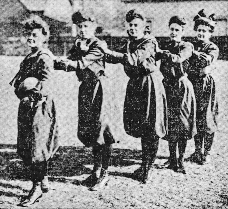 Five girls stand in a line, each with an arm resting on the shoulder of the girl in front of her. The first girl in the line holds a basketball.