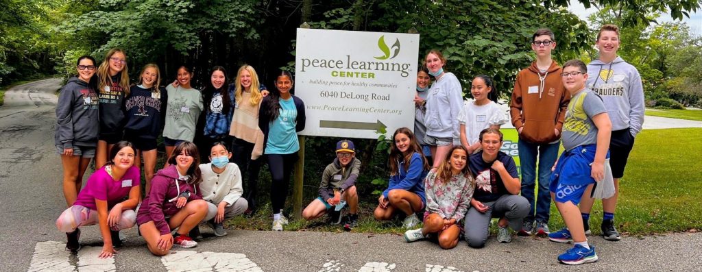 Several teenagers gather together outside around the Peace Learning Center sign for a group photo.