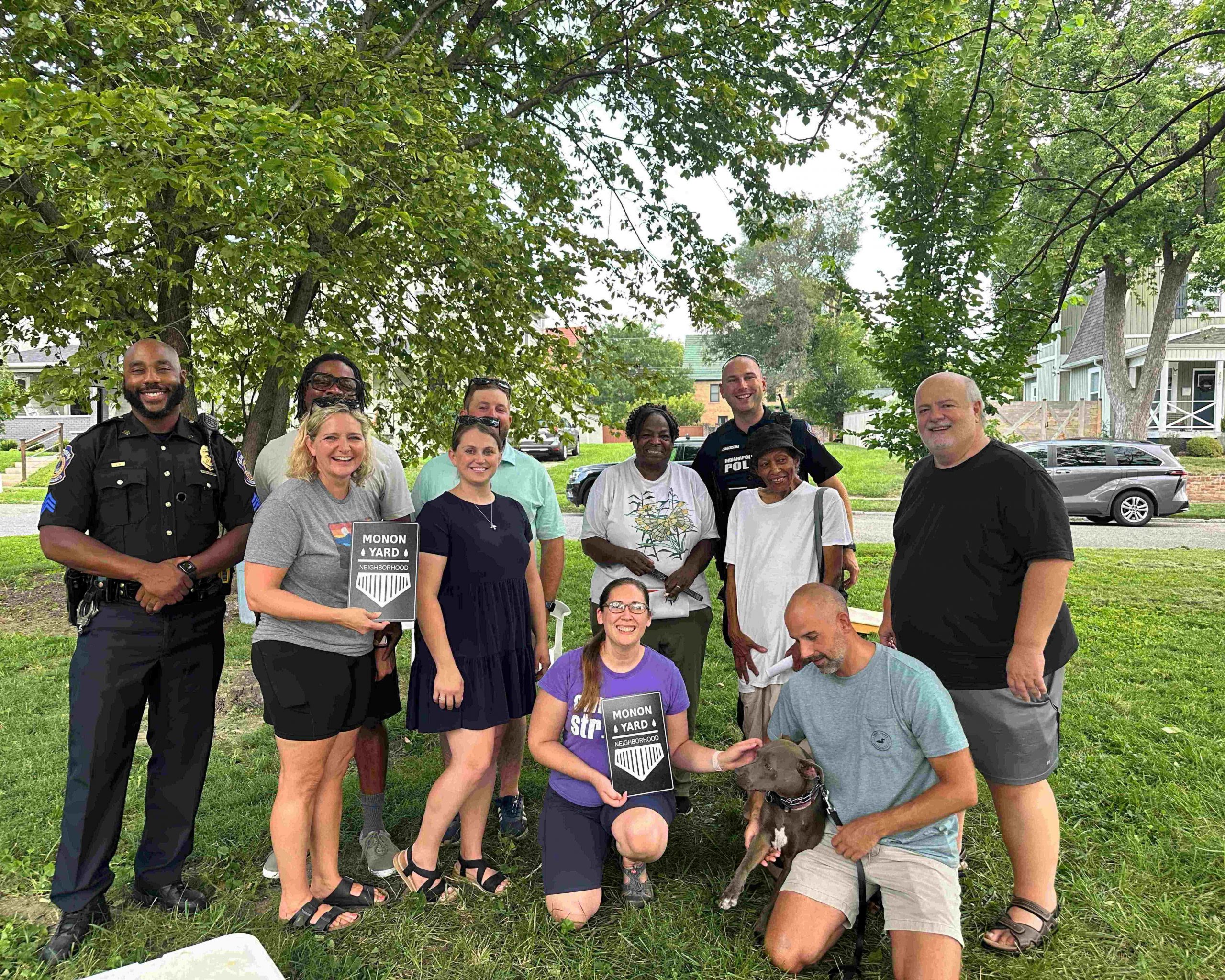 A group of people are gathered together outside. Two people hold up signs that read "Monon Yard Neighborhood.: