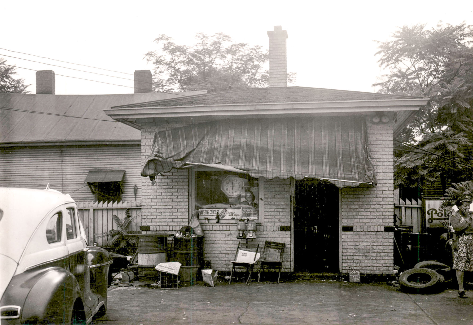 A small, brick building with a fabric awning over the door. A car is parked in front of the building.