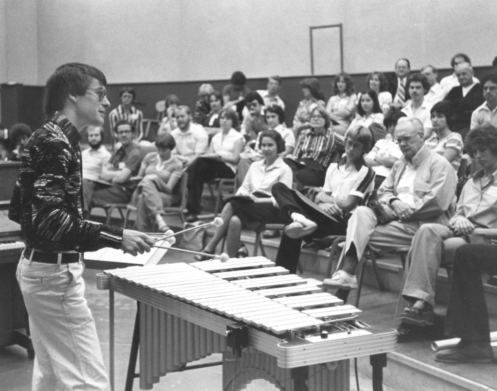 A man plays a xylophone in front of a group of people.