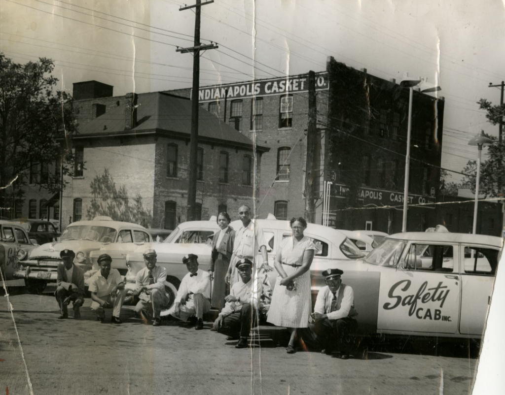 A group of staff line up in front of several parked taxi cabs. The cabs are branded "Safety CAB INC."