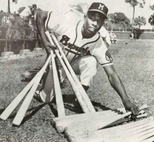 A young Hank Aaron poses in his Braves uniform. He is holding several bats.