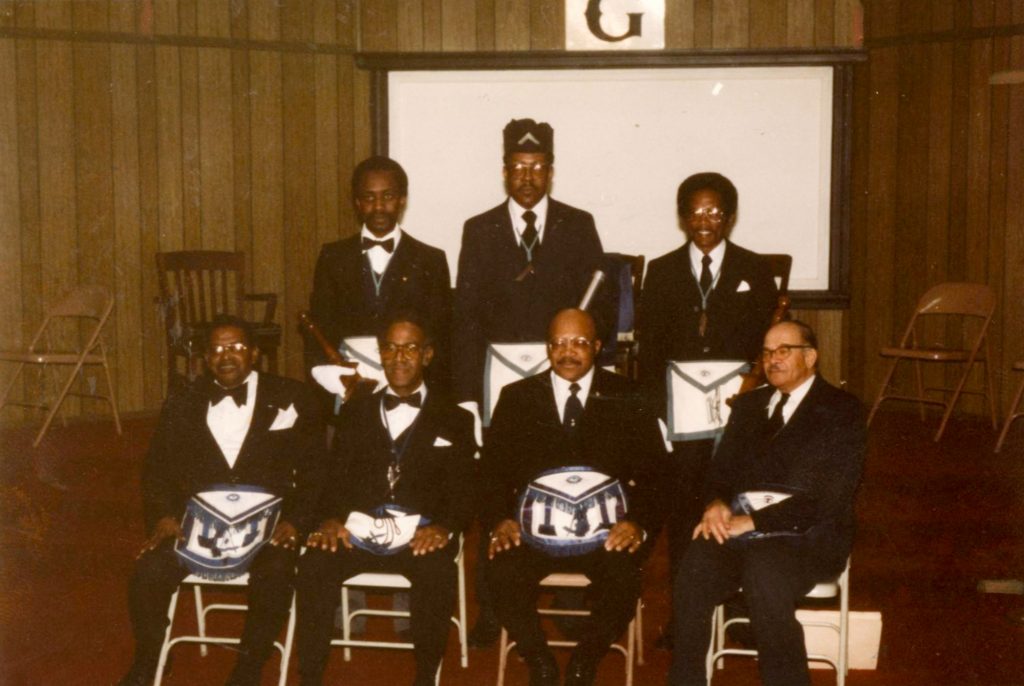 A group of seven Black men pose together. They are wearing suits and masonic regalia.