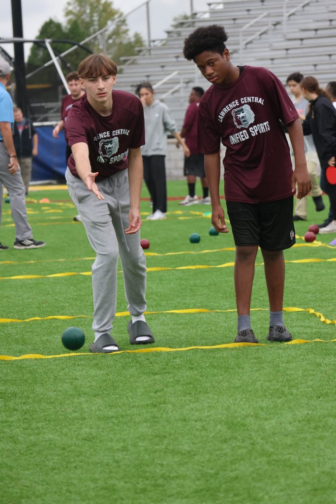 A young man throws a bocce ball while his partner watches.