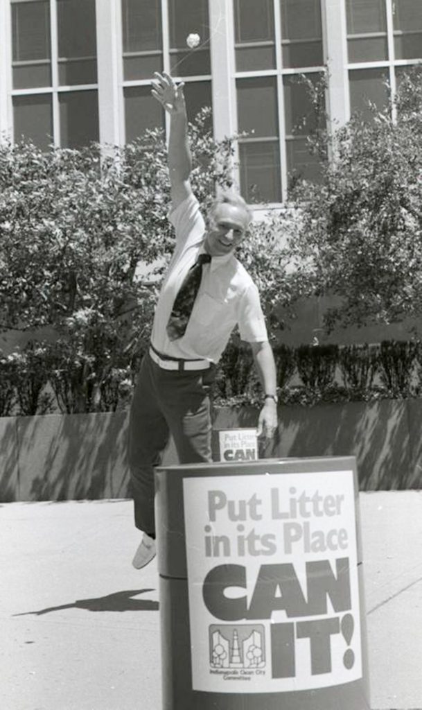 A man throws a piece of litter into a garbage can. The can has a large decal that reads "Put litter in its place. Can it!"