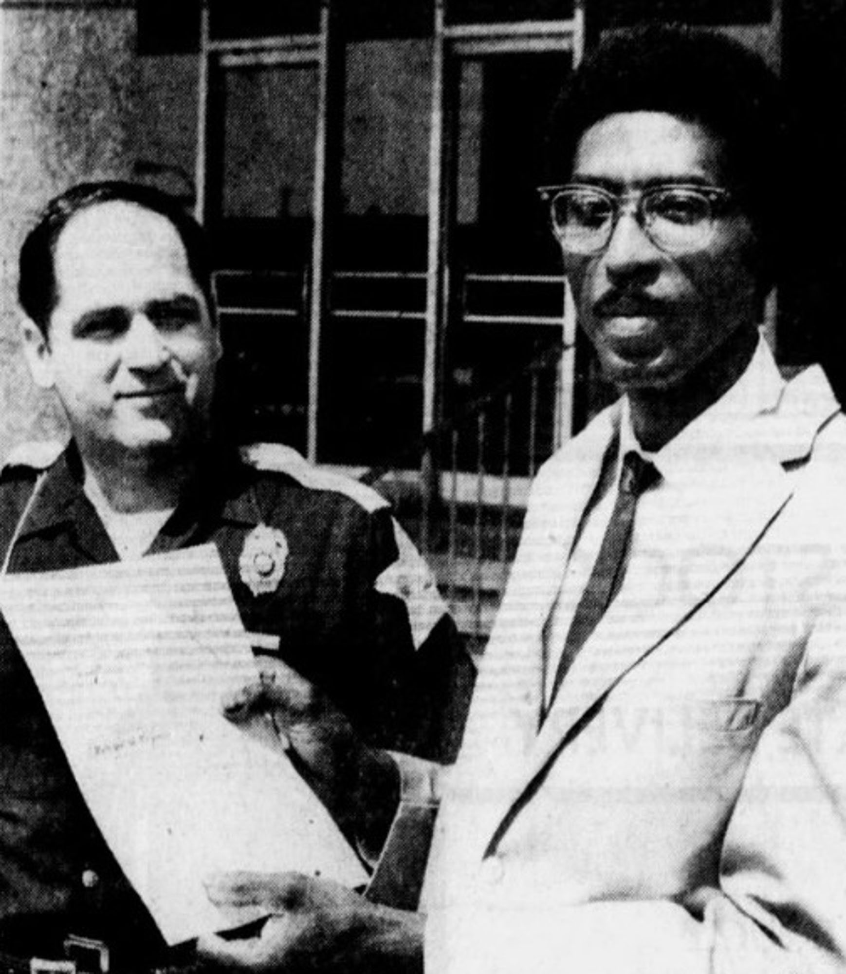 A man holds up a form. A police officer stands next to him.