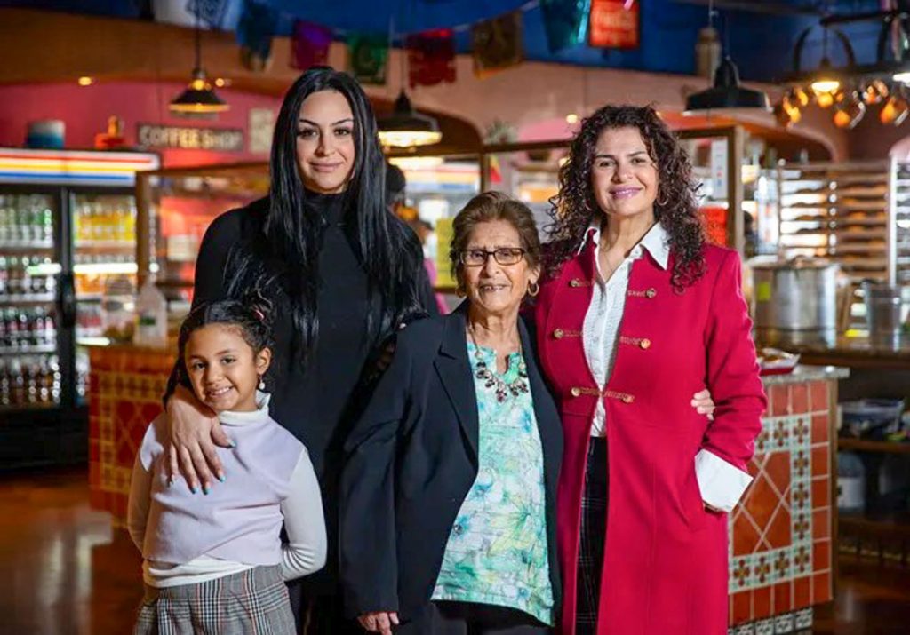 Three women and a young girl stand together in their bakery, They represent multiple generations.