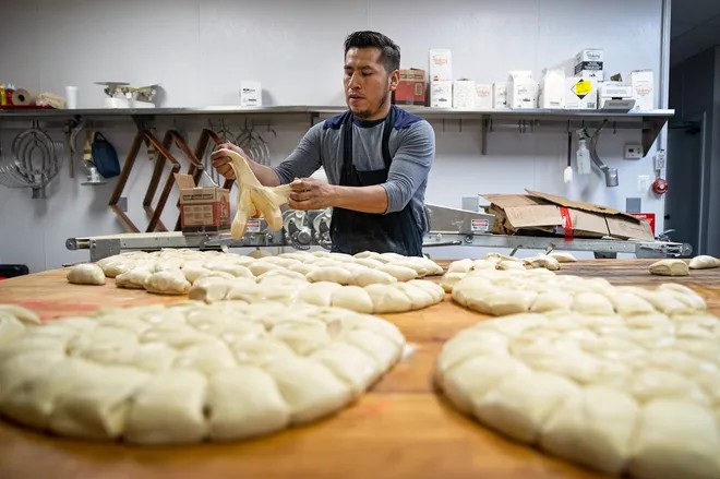 A man shapes balls of dough in an industrial kitchen.