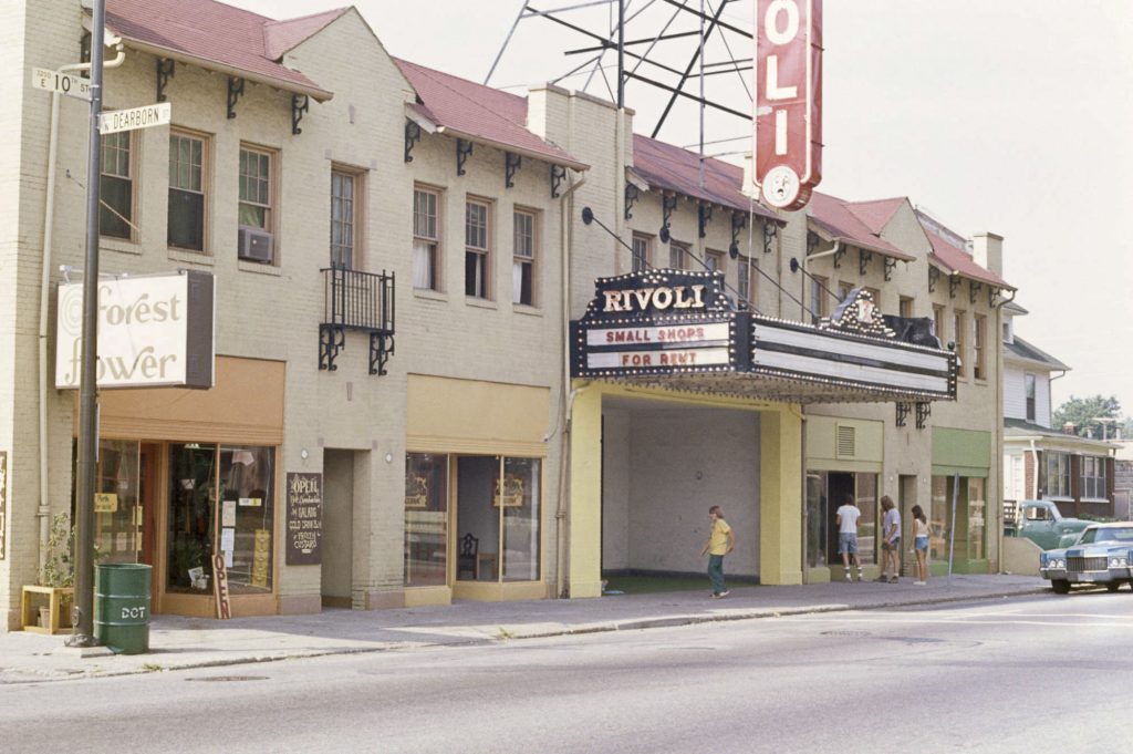 Two story stucco building with commercial storefronts and apartments on second floor. Movie marquee over main entrance.