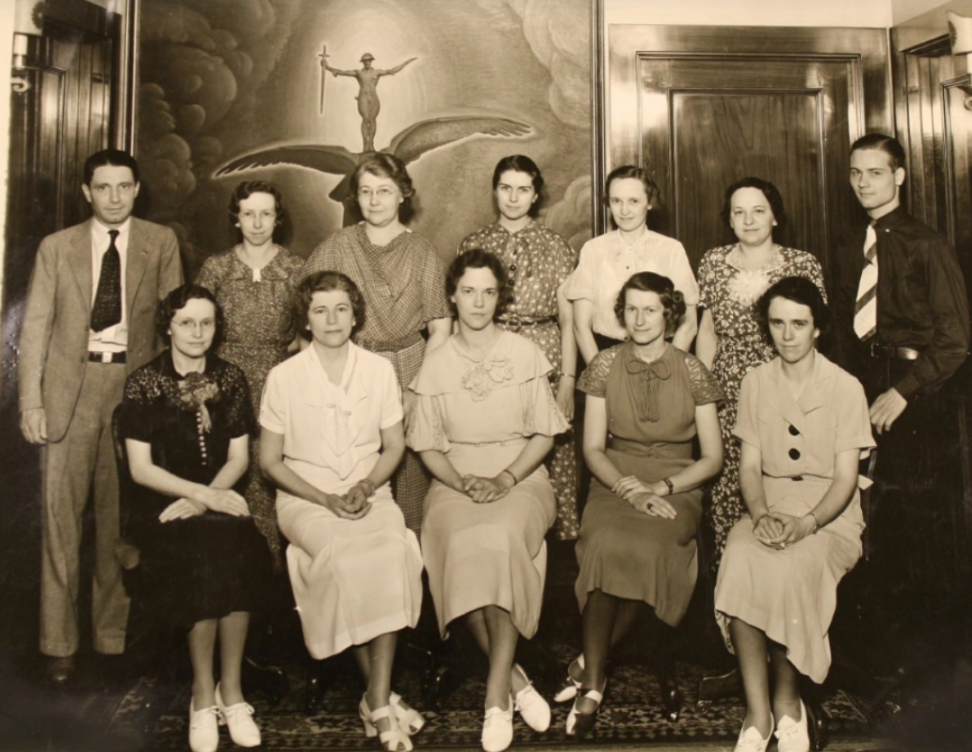 Historic group portrait showing twelve adults posed indoors in two rows.