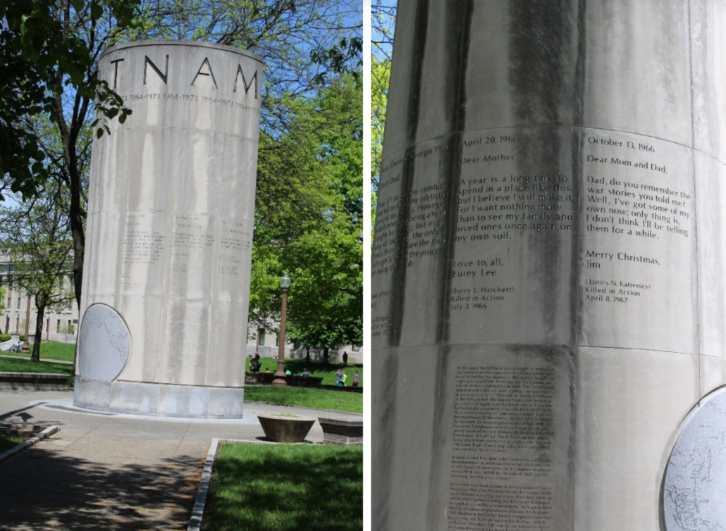 Side-by-side color photographs of the Vietnam War Memorial in a park setting. The left image shows a tall cylindrical concrete monument engraved with the letters “TNAM” near the top and surrounded by trees, lawns, and paved walkways. The right image is a close-up of the monument's surface, showing engraved excerpts from letters written by service members, along with additional inscriptions and a circular map element near the base. The memorial stands among landscaped grounds under a clear blue sky.