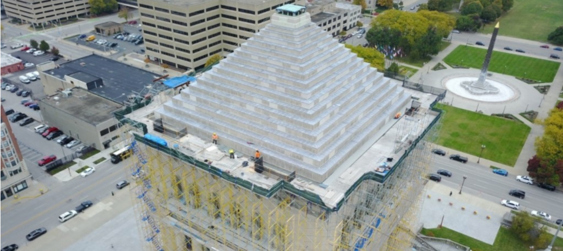 Aerial view of the Indiana World War Memorial during a restoration project. The monument’s stepped pyramid roof is surrounded by extensive scaffolding, with several workers visible on the structure.